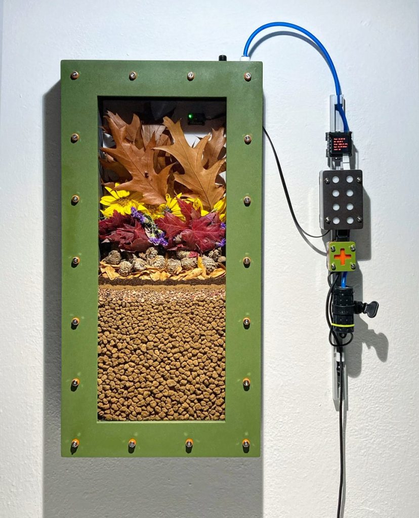 
Moonwort Studio. Coulee Region -1983, 2023. Edaphotron: watertight enclosure, electronic gas sensor, microcontroller, bonsai gravel, plant parts, soil invertebrates and soil microflora. 15" X 4" X 23" (38cm X 8cm X 58cm).